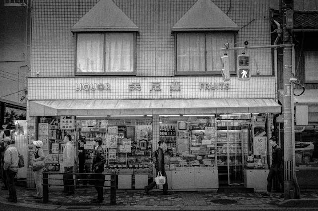Photograph of Store Selling Liquor and Fruits and a Line of Patrons